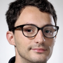 A headshot of a person wearing glasses with short, dark hair and a slight smile, set against a plain background.