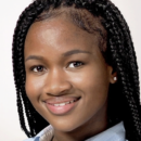 Headshot of a smiling person with braided hair, wearing a light-colored collared shirt, against a neutral background.