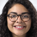 Headshot of a person with curly hair and glasses, smiling at the camera.