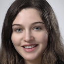 A headshot of a person with long brown hair and blue eyes, smiling against a neutral background.