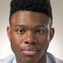 Headshot of a person with short, textured hair, wearing a light-colored shirt, facing forward against a neutral background.