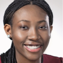 Headshot of a person smiling, with braided hair and wearing a maroon top and stud earrings.