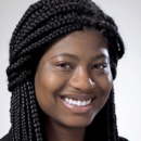 Headshot of a person smiling with long braided hair against a neutral background.