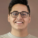 Headshot of a person wearing glasses and a light-colored shirt, with a neutral brown background. The person is smiling.