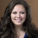 A headshot of a person with long wavy hair, smiling against a plain brown background.