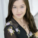 A headshot of a person with long hair, wearing a floral-patterned black top and a necklace, looking directly at the camera.