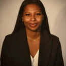 A professional headshot of a person wearing a dark blazer and white top, smiling against a neutral background.