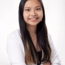 A person with long hair and a friendly smile, wearing a white blazer and black top, posing with arms crossed against a plain background. Headshot.