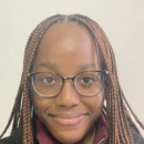 A headshot of a person with glasses and braided hair, smiling slightly against a light background.