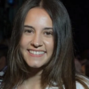 A person with long, dark hair smiling, wearing a white top and a small necklace, captured in a headshot.