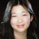 Headshot of a person with long dark hair and a slight smile, set against a dark background.