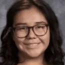 A headshot of a person with long dark hair, wearing glasses and smiling, against a neutral background.