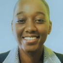 Headshot of a person smiling, wearing a striped collared shirt and dark jacket, against a light blue background.