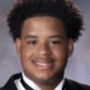 A headshot of a person wearing a formal black suit with a white shirt and black bow tie, smiling in front of a neutral background.