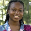 Headshot of a person smiling outdoors, wearing a floral-patterned blouse. The background is a blurred green, possibly indicating a garden or park setting.