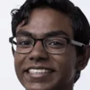 Headshot of a person with glasses and dark hair, smiling in front of a plain background.