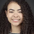 A headshot of a person with curly hair, smiling at the camera, against a dark background.