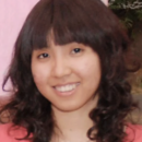 Headshot of a person with shoulder-length wavy hair, smiling, wearing a necklace and a pink top.