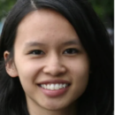 A headshot of a person with long dark hair smiling, set against a blurred outdoor background.