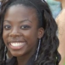 A headshot of a smiling person with long, curly hair wearing earrings.