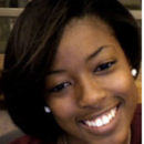 A headshot of a smiling person with short, dark hair, wearing earrings. The background appears to be an indoor setting.