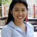 A headshot of a person smiling, standing outdoors in front of a playground with trees and a building in the background.