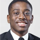 A headshot of a person smiling, wearing a dark suit and tie, against a plain background.