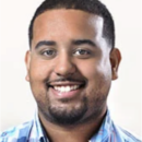 This is a headshot of a person smiling, wearing a blue plaid shirt, with short hair and a trimmed beard.