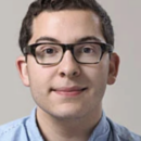 A headshot of a person wearing glasses and a light blue shirt, with a neutral background.