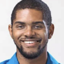 A person smiling in a headshot, wearing a blue collared shirt, with short hair and a beard, set against a plain background.