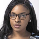 A headshot of a person wearing glasses and pearl earrings with long, dark hair. The individual is dressed in a textured top.