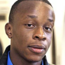 Headshot of a person wearing a blue shirt and a black jacket, looking towards the camera with a neutral expression.