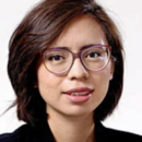 A headshot of a person with short, dark hair wearing glasses and a patterned top, set against a plain background.