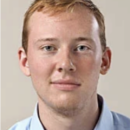 Headshot of a person with short, light brown hair, wearing a light blue collared shirt, and a neutral expression.