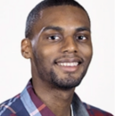 Headshot of a person smiling, wearing a plaid shirt with a light background.