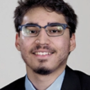 Headshot of a person wearing glasses and a suit, with short dark hair and facial hair, smiling at the camera.