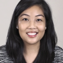 Headshot of a smiling person with long, dark hair, wearing a striped top and earrings. The background is plain.