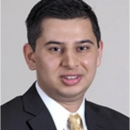 A headshot of a person wearing a black suit, white shirt, and a gold tie.