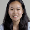 Headshot of a person with long, dark hair, smiling, against a neutral background.