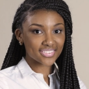 Headshot of a person with long braided hair, smiling, wearing a white collared shirt, set against a plain background.