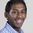 Headshot of a person smiling, wearing a checkered shirt, against a plain background.