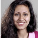 A headshot of a person with long, dark hair, smiling at the camera, wearing a pink collared shirt.