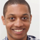 A headshot of a person smiling, wearing a checkered shirt, with short hair.