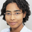 Headshot of a person with curly hair, glasses, and a slight smile, wearing a light-colored shirt.