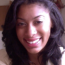 A headshot of a smiling person with long, dark hair, wearing a light-colored top, taken indoors.