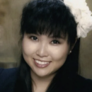 A portrait of a person smiling, with long dark hair and a large white flower in their hair.