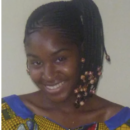 A person smiling with braided hair adorned with beads, wearing a colorful patterned garment.