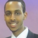 A headshot of a person in a suit and tie, smiling against a purple background.