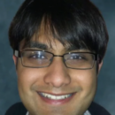 A headshot of a person with short dark hair, glasses, and a slight smile against a blurred background.