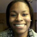 Headshot of a smiling person with short hair, wearing a patterned scarf and pearl earrings, against an indoor background.